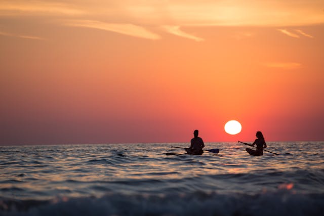 two people paddling in the ocean at sunset